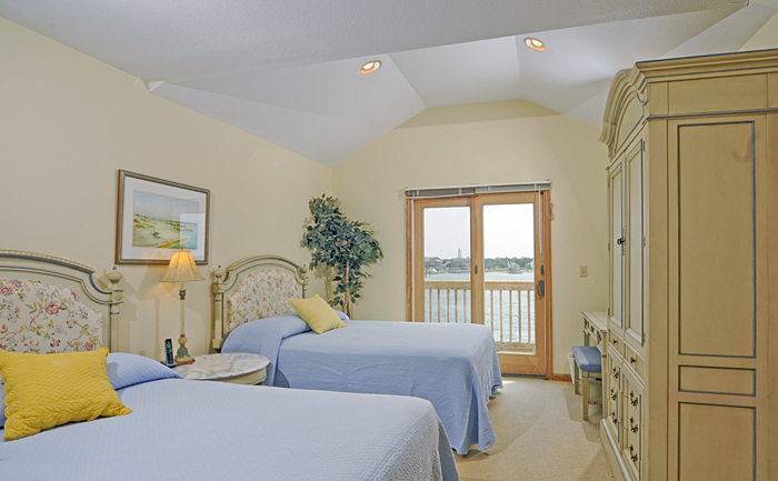 Bedroom with 2 double beds, armoire, nightstand, desk and chair, sliding door to waterfront balcony